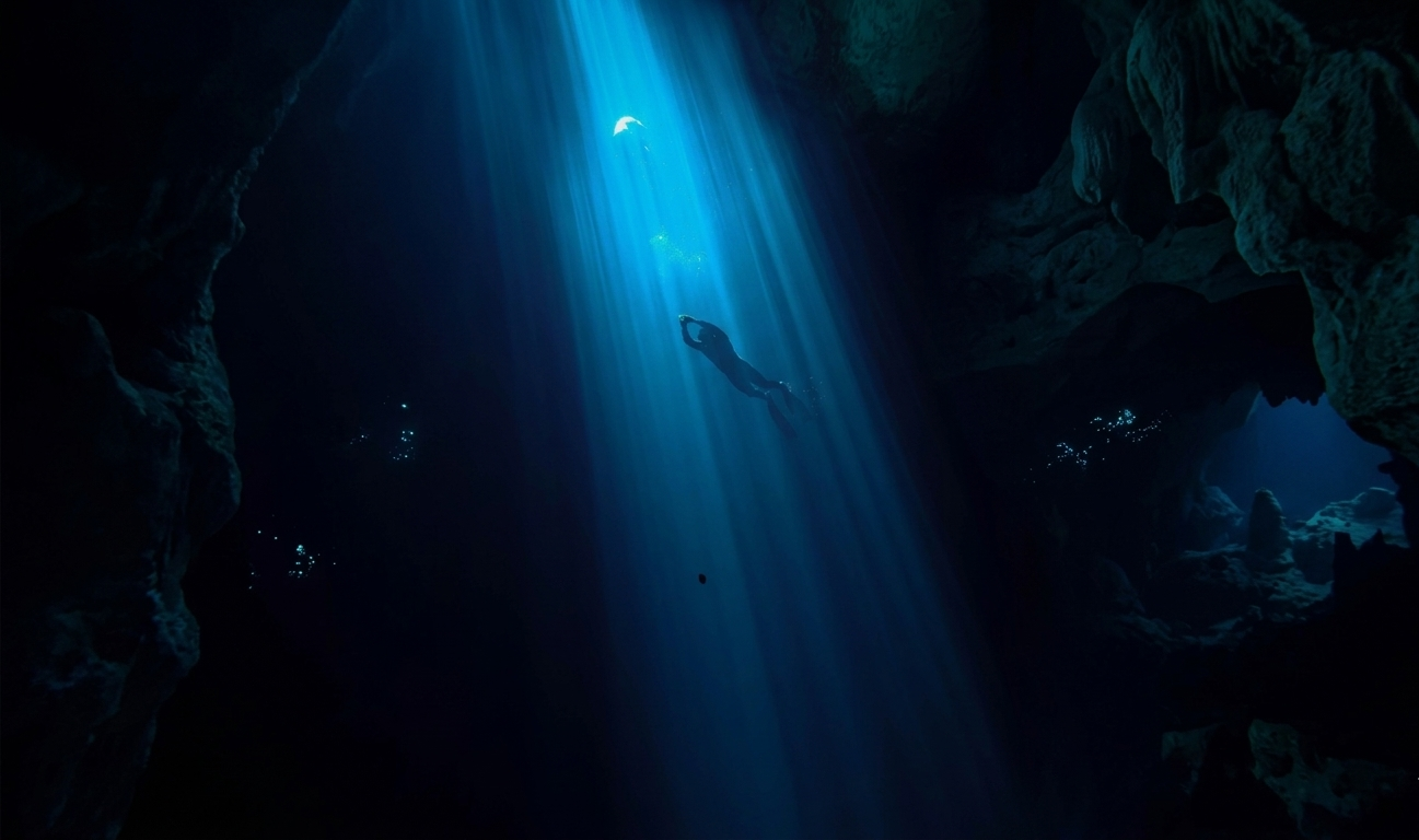 Persona practicando Snorkel en Riviera Maya en una cueva submarina, fomentando el turismo de aventura. descendiendo a pulmón entre formaciones rocosas y la luz filtrada que ilumina el agua azul para aquellos que poseen un espíritu aventurero.