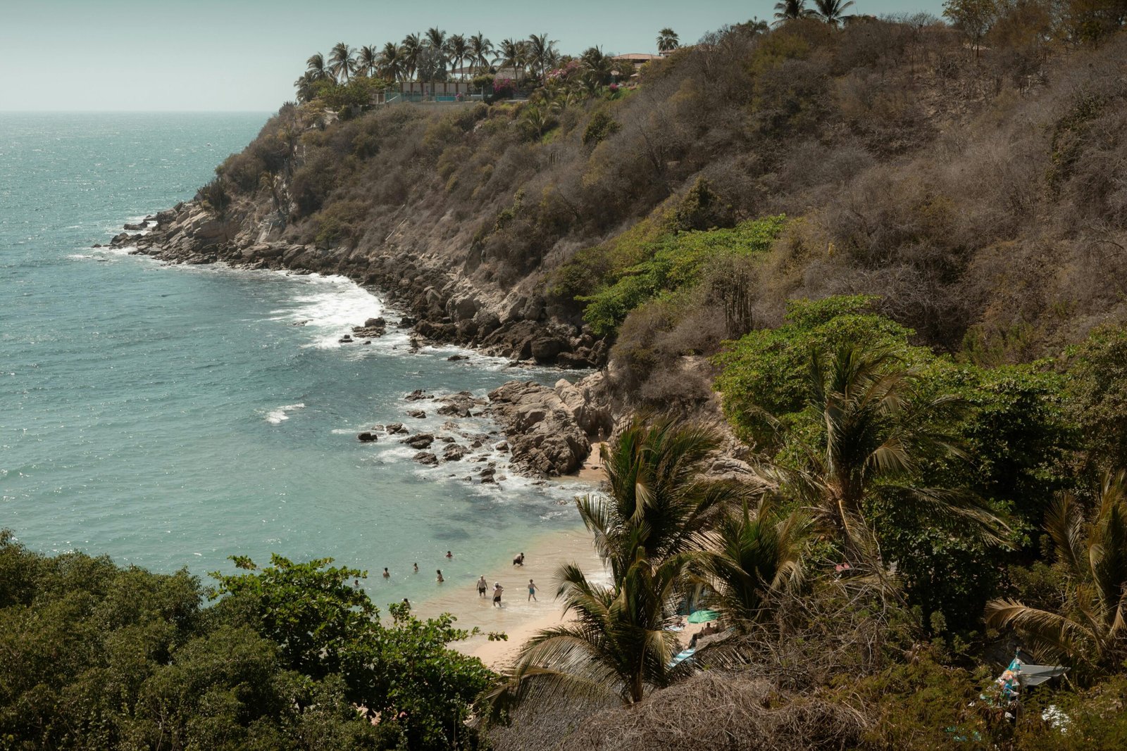 Vista panorámica de una playa virgen en Puerto Escondido, Oaxaca, con acantilados rocosos, vegetación tropical y mar color turquesa