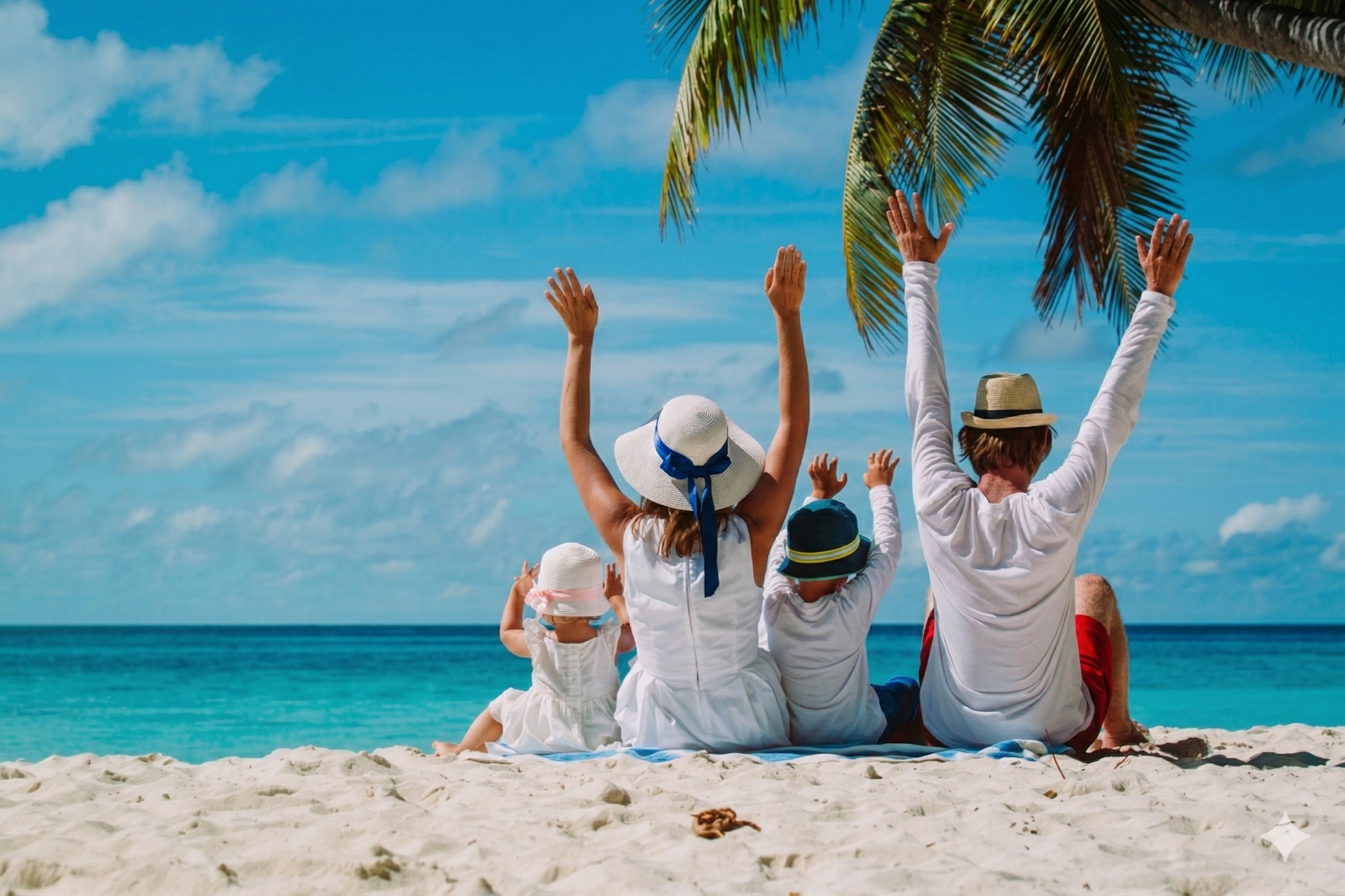 Familia de cuatro integrantes (mamá, papá, hija e hijo) sentada de espaldas en una playa de arena blanca bajo una palmera en la Riviera Maya, levantando los brazos de felicidad frente al mar turquesa.