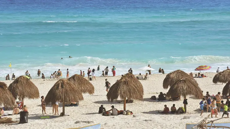 Vista panorámica de Playa Delfines en Cancún, con arena blanca, mar turquesa y turistas en primer plano