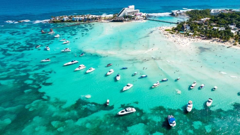 Vista de la playa Isla Mujeres con barcos y yates anclados en las aguas cristalinas con el hotel Mia Reef al fondo